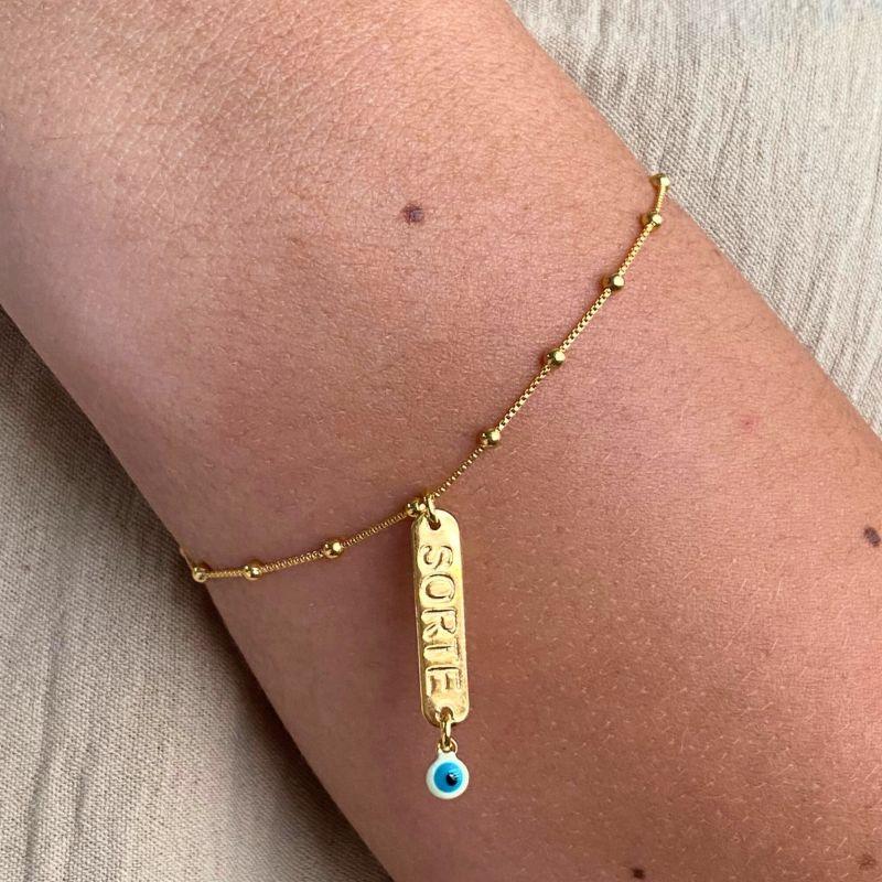PULSEIRA COM 15 BOLINHAS PP E COM UMA PLACA ESCRITO SORTE E OLHO GREGO